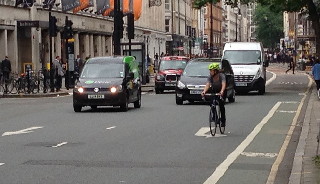 A cyclist takes the lane to beat cars to the next stoplight. Tottenham Court Rd.